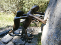 Dos personas de bronce y granito haciendo rodar por el puente una piedra pesada hacia el río.